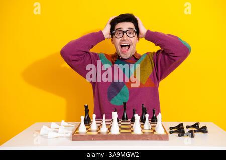 Excité jeune homme en pull coloré jouant aux échecs sur un fond jaune vibrant Banque D'Images