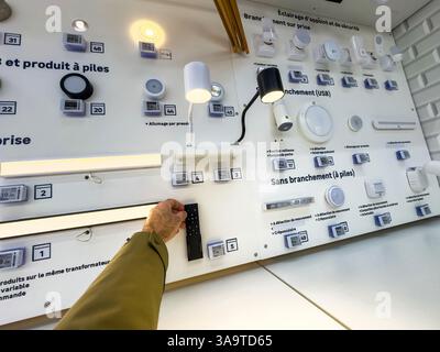 Paris, France - 27 mars 2025 : un panneau de démonstration d'éclairage mural dans un magasin de bricolage français montre diverses lumières enfichables et alimentées par piles, avec une main i. Banque D'Images