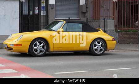 Bologne, Italie 7 février 2025 Shiny Speed Yellow Porsche 993 Carrera 4 Cabriolet garée dans une rue de la ville près d'un passage rouge Banque D'Images