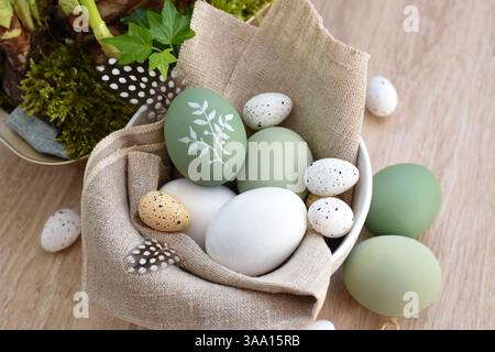 Oeufs de pâques élégants décorés dans un bol blanc sur toile de lin sur une table en bois clair. Vue de dessus Banque D'Images