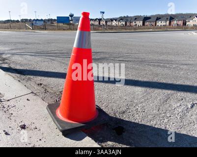 Un cône de circulation accrocheur se trouve stoïquement sur la toile de fond de nouvelles maisons de banlieue, marquant discrètement les espaces de prudence et de changement futur Banque D'Images