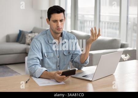 L'homme regarde la calculatrice avec une expression perplexe et stressée Banque D'Images