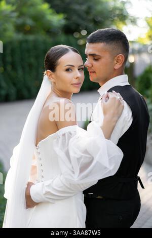 Couple de jeunes mariés se tenant la main et s'embrassant dans un parc, célébrant leur amour et leur engagement lors de leur cérémonie de mariage Banque D'Images