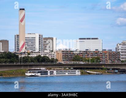 Bâle, Suisse - 17 août 2024 : un bateau de croisière fluviale navigue sous un pont dans une zone urbaine avec des bâtiments modernes, y compris une grande cheminée et un Banque D'Images
