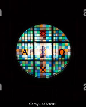 Michaelbeuern, Autriche - 22 octobre 2024 : un vitrail circulaire avec des motifs géométriques colorés et les lettres Alpha et Omega. Banque D'Images