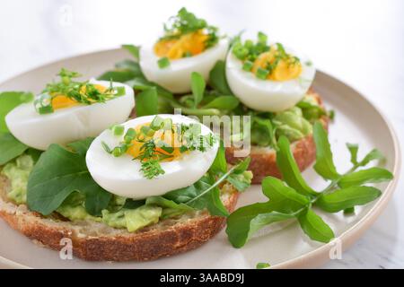 Petit déjeuner avocat toast sur pain rustique croustillant avec des œufs durs garnis d'herbes en gros plan Banque D'Images