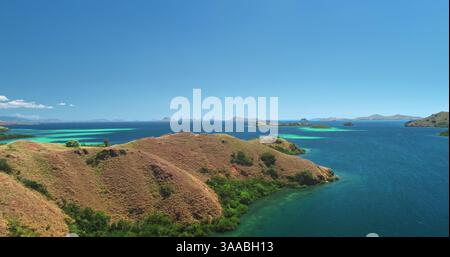Vue aérienne de l'île de Padar dans le parc national de Komodo, en Indonésie, mettant en valeur les superbes baies turquoises, les collines verdoyantes et la vaste étendue de l'océan sous un ciel bleu vibrant Banque D'Images
