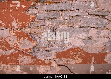 Mur fissuré au charme rustique. Gros plan détaillé d'un mur altéré avec de la peinture rouge écaillée, révélant des couches de plâtre et de briques en dessous. Copier Banque D'Images