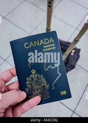 Passeport canadien détenu par une personne, avec une valise en arrière-plan à un aéroport. Parfait pour les voyages, l'immigration et les thèmes identitaires. Banque D'Images