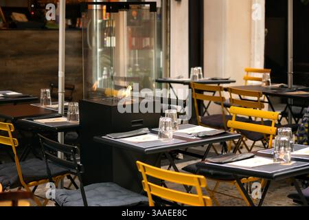 Le restaurant extérieur est équipé de chaises noires et jaunes, de tables et d'une cheminée moderne vitrée. Ambiance chaleureuse du soir dans un cadre européen Banque D'Images