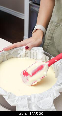 Pâte à gâteau délicieusement lisse mélangée avec une spatule rouge dans un moule à gâteau rond noir. Banque D'Images
