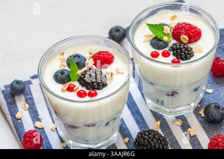 Yaourt grec avec des baies fraîches, de l'avoine et de la menthe dans des verres sur fond blanc. Yaourt aux myrtilles, framboises, mûres et granola. En bonne santé Banque D'Images