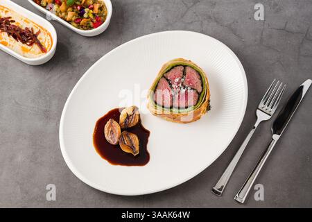 Assiette moderne de bœuf Wellington, échalotes caramélisées et sauce foncée Banque D'Images