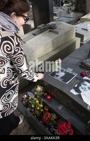 Femme dépose une fleur sur la tombe de la chanteuse Edith Piaf au cimetière du Père-Lachaise, Paris, France au début du printemps Banque D'Images