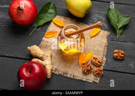 Pot de miel doux avec noix, pommes et grenade sur fond en bois noir Banque D'Images