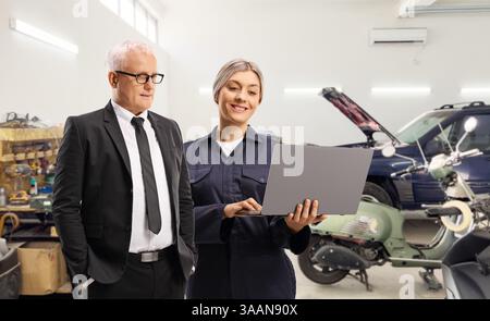 Femme mécanicien de réparation automobile montrant un ordinateur portable à un homme dans un garage de voiture Banque D'Images