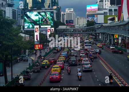 Cette image vibrante du soir capture la circulation animée sur Ratchadamri Road, Bangkok, Thaïlande, sous un ciel sombre et nuageux. Un mélange de voitures, taxis, tuk-t Banque D'Images