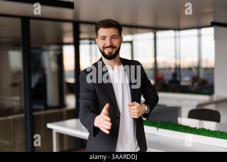 Portrait de l'homme d'affaires accueillant le nouvel employé à son équipe d'affaires et l'entreprise, donnant la main en avant dans le bureau moderne avec des collègues dans le backgroun Banque D'Images