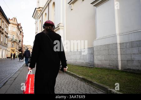 Lviv, Ukraine - 31 mars 2025 : une personne se promène dans une charmante rue historique avec un sac à provisions à la main à Lviv, en Ukraine. Banque D'Images