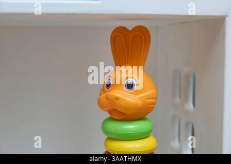 Un jouet lapin vibrant avec de grands yeux se trouve au sommet d'anneaux empilés colorés dans un cadre minimaliste. Parfait pour les jeux d'enfants, il ajoute plaisir et fantaisie à Banque D'Images