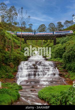 Un train panoramique traverse un pont métallique au-dessus des cascades de Nanu Oya au Sri Lanka, entouré de verdure luxuriante et de plantations de thé, créant ainsi Banque D'Images