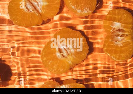 Moitiés de mandarine fraîche pelées dans l'eau, éclaboussures d'eau, vue de dessus. Banque D'Images