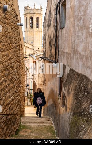 Femme touristique descendant une rue très étroite avec l'église du village médiéval en arrière-plan, Cretas, Teruel. Banque D'Images