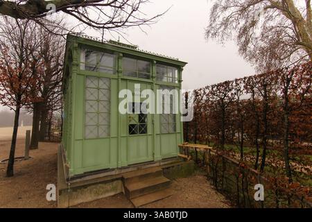 Toilettes extérieures décoratives avec verdure et haies automnales, situées dans un parc paisible pendant une journée nuageuse. Présente des couleurs naturelles et un arc simple Banque D'Images