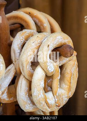Un gros plan de plusieurs bretzels artisanaux fraîchement cuits suspendus sur un support en bois. Banque D'Images