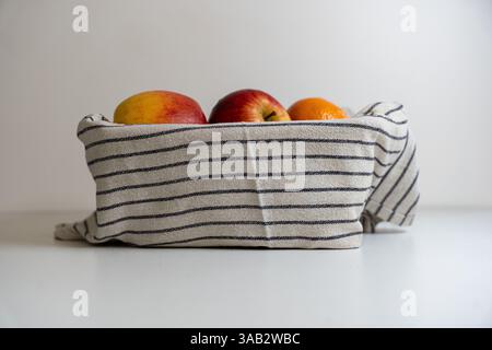Un panier de pommes recouvert d'un torchon sur fond blanc. Banque D'Images