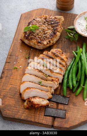 Côtelette de porc grillée ou poulet tranché sur une planche à découper servi avec des haricots verts Banque D'Images