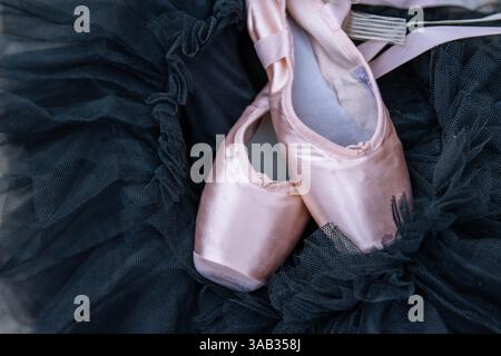 Gros plan des chaussures de pointe de ballet rose reposant sur le Tutu en mousseline noire. Deux pantoufles de ballet beiges sur le fond sombre. Concept minimaliste. Copier Banque D'Images