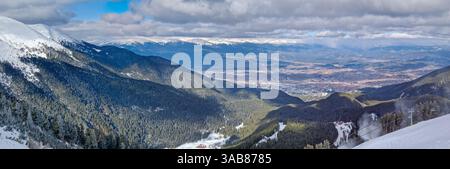 Vue panoramique sur la belle ville de Bansko vu derrière la forêt à feuilles persistantes et les collines de montagne à l'horizon Banque D'Images