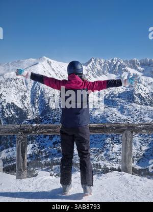 Vue arrière femme skieuse sur le sommet de la montagne debout avec les bras grands ouverts face à la neige couverte pics Pirin à la station de ski de Bansko, Bulgarie. Scène avec un fe Banque D'Images