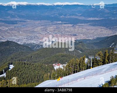 Station de ski Bansko dans les montagnes Pirin avec télésièges se déplaçant au-dessus des pistes enneigées et une belle vue sur la colline de la vieille ville Banque D'Images