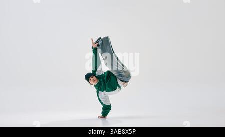 Performant, habillé rétro, saisissant pose dynamique à une main avec les jambes en suspension, mettant en valeur la force sur fond blanc de studio. Banque D'Images