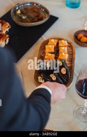 Un invité en tenue habillée va chercher un plateau en bois magnifiquement arrangé rempli de petits pains bao au poulpe et de hors-d'œuvre brun doré, sur une étiquette raffinée Banque D'Images