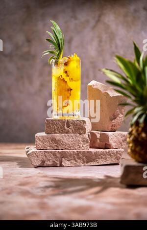 Une boisson à l'ananas soigneusement préparée, réfrigérée et servie dans un grand verre, garnie d'une feuille d'ananas fraîche, élégamment exposée sur un STO empilé Banque D'Images