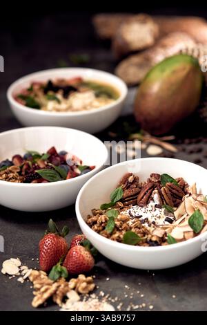 Trois bols naturels remplis d'options de petit-déjeuner délicieuses et nutritives, avec des fruits frais, des noix, des graines et des légumes verts. Fraises et pain dedans Banque D'Images