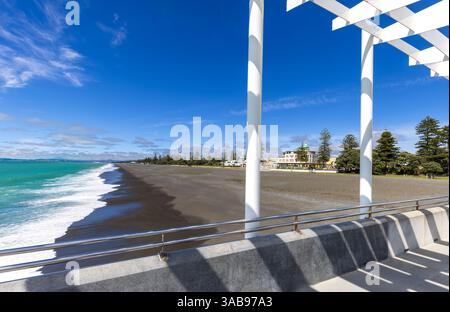 Surplombant la rive sablonneuse de Hawke Bay, cette image capture l'architecture art déco distinctive de Napier bordant la promenade dynamique du front de mer. Banque D'Images