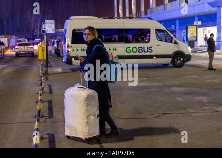 Voyageur avec bagages la nuit devant la sortie de l'aéroport de Manas et GoBus Shuttle bus au Kirghizistan Banque D'Images