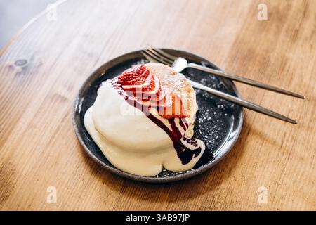 Crêpes japonaises moelleuses garnies de fraises fraîches, d'un filet de crème et de sauce aux baies. Servi sur une assiette sombre, ce plat de petit déjeuner invitant est Banque D'Images