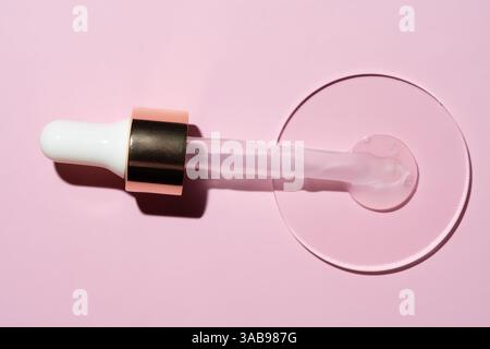 Pour voir un compte-gouttes contenant du sérum d'or 24K reposant sur une boîte de Pétri, placez-le sur un fond rose pâle. Idéal pour les promotions beauté et soins de la peau. Banque D'Images