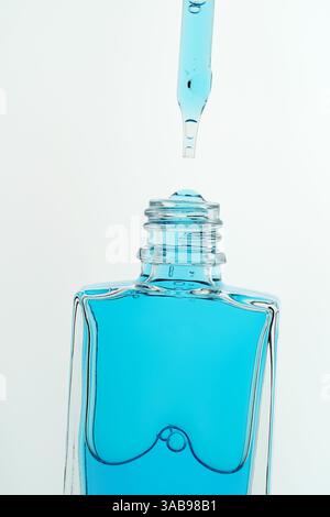 Gros plan d'une pipette avec un liquide bleu en suspension au-dessus d'un flacon cosmétique. L'image capture le moment d'anticipation avant que le liquide ne tombe Banque D'Images