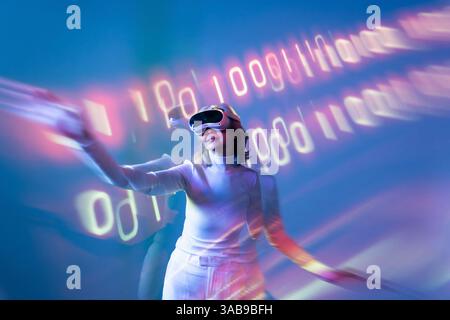 Une femme asiatique âgée fait l'expérience de la métaverse en utilisant la technologie de réalité virtuelle, s'engageant dans des environnements numériques tout en portant un casque VR dans un Banque D'Images