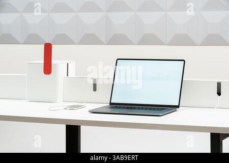 Un espace de travail épuré et minimaliste au bureau dispose d'un ordinateur portable et d'un smartphone sur un bureau blanc, idéal pour la productivité. La configuration est moderne, avec une ligne propre Banque D'Images