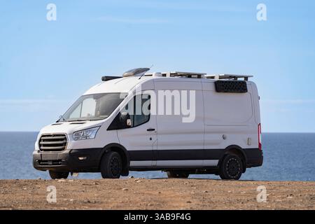 Un camping-car blanc garé sur un paysage rocheux au bord de l'océan sous un ciel bleu clair à Fuerteventura, îles Canaries, Espagne, symbolisant l'aventure Banque D'Images