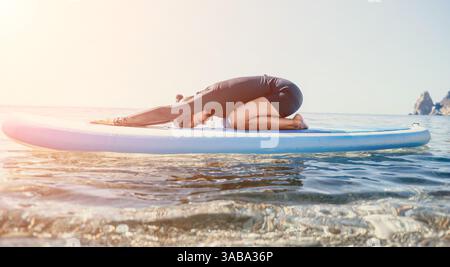 Yoga Paddleboard exercice aquatique - homme pratiquant le yoga sur paddleboard dans l'eau calme par une journée ensoleillée. Banque D'Images