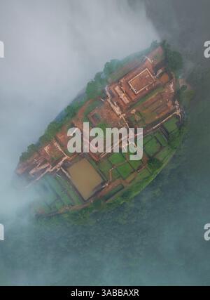 Une vue aérienne de Sigiriya, l'ancienne forteresse rocheuse au Sri Lanka, émergeant à travers la brume, mettant en valeur ses jardins luxuriants et ses ruines historiques au sommet de la Banque D'Images