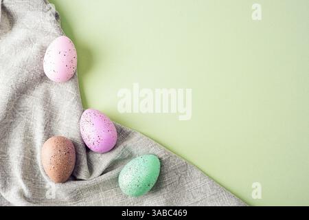 Oeufs de Pâques pastel mouchetés sur tissu de lin sur fond vert. Concept de Pâques. Vue de dessus, pose à plat, espace de copie. Banque D'Images